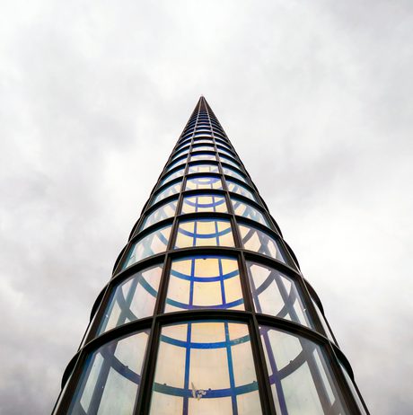 Looking up towards a tall pointed tower, with glass panels