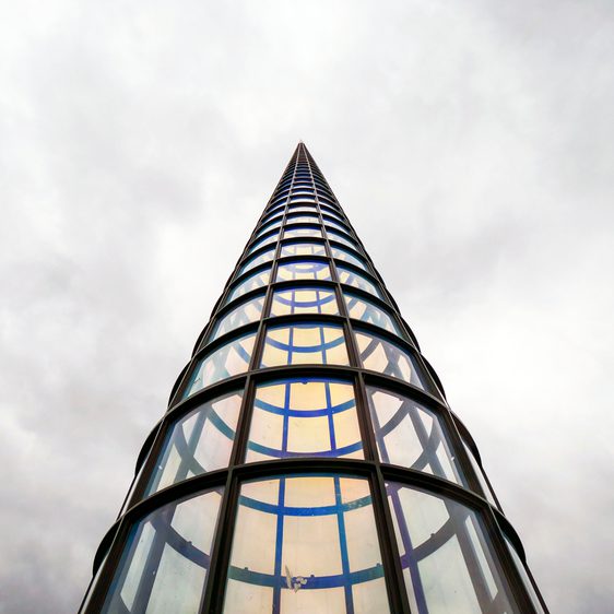 Looking up towards a tall pointed tower, with glass panels