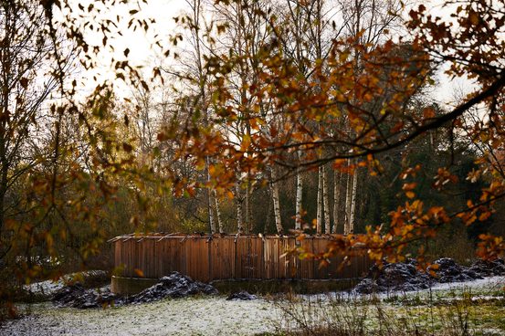 A roofless wooden pavilion surrounded by trees.