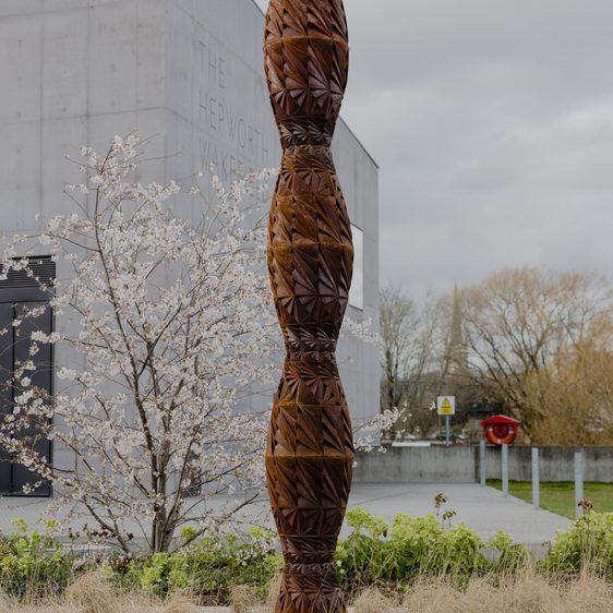 A tall thin bronze sculpture in a garden