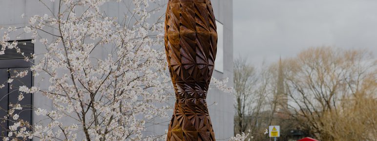 A tall thin bronze sculpture in a garden
