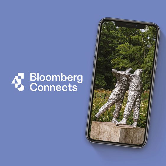 An image of a mobile phone displaying a photograph of a sculpture depicting two embracing figures. The image has a pale blue background with white text: Bloomberg Connects