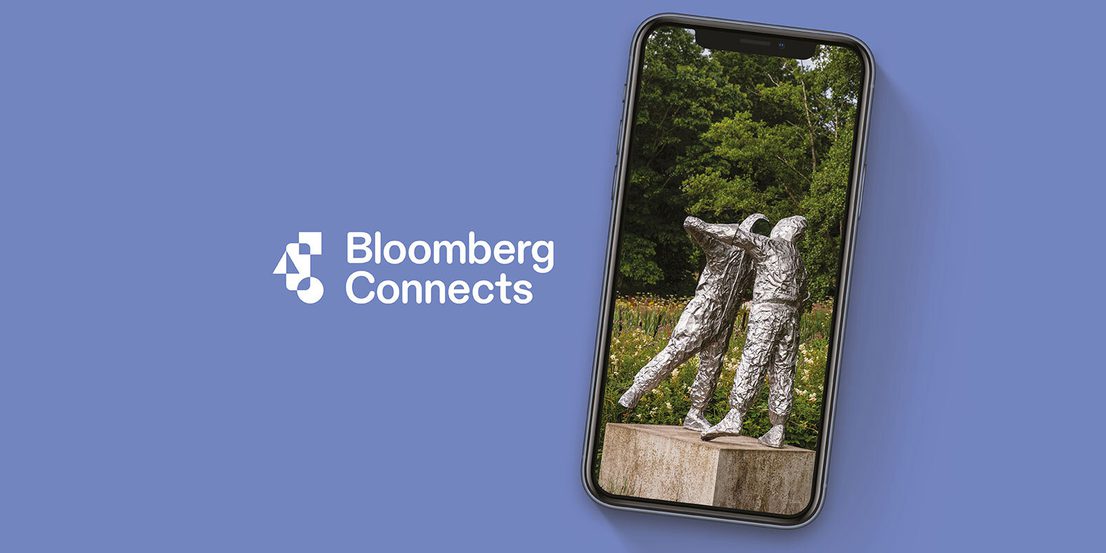 An image of a mobile phone displaying a photograph of a sculpture depicting two embracing figures. The image has a pale blue background with white text: Bloomberg Connects