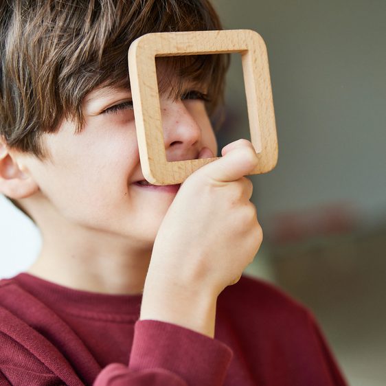 A child holding a square wooden viewfinder to his face.