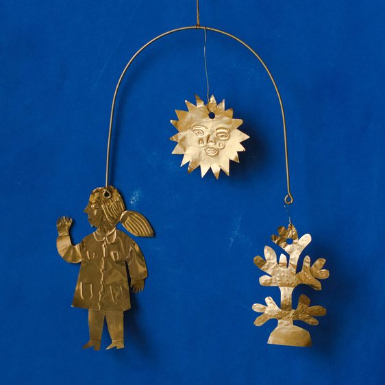 A folk-art style mobile made from shiny gold metal, featuring a person, sun and flower, against a blue background.