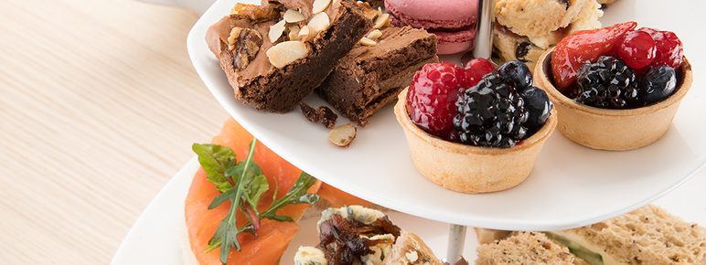 A two-tier cake stand, filled with cakes, pastries and finger sandwiches.