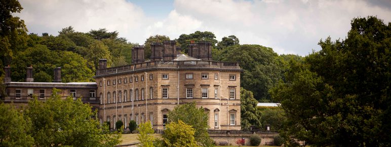 A large historic hall surrounded by trees in YSP parkland.