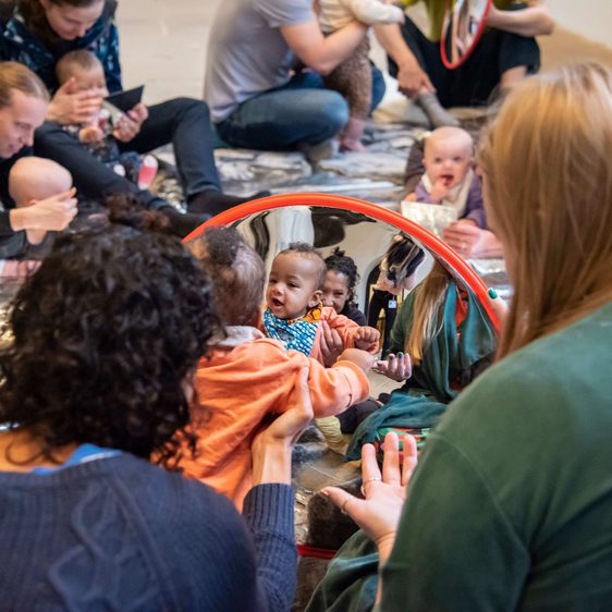 A group of adults and infants interacting with a mirror.