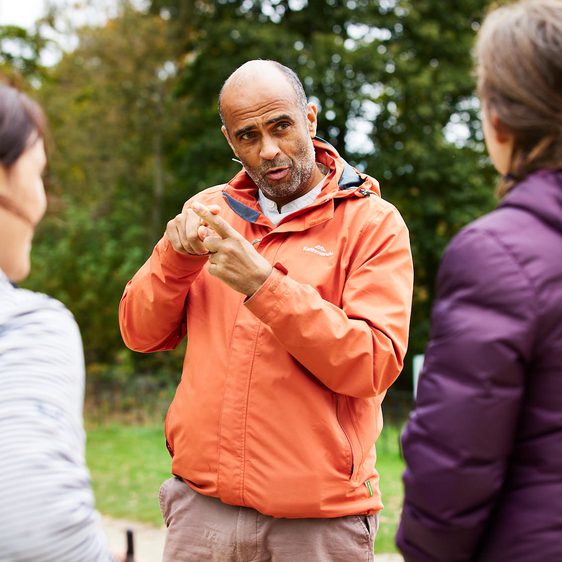 A man in an orange coat doing sign language outdoors