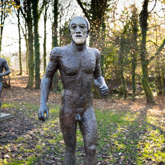 Three nude male bronze figures with white painted faces, displayed outdoors.