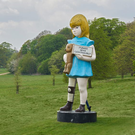 Sculpture of a young girl holding a teddy bear and a charity box, among saplings in YSP parkland.
