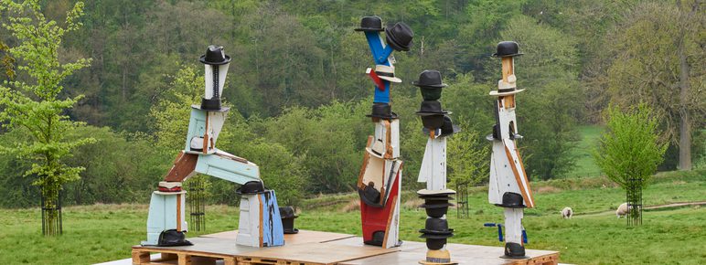 Four sculptures with fedora, boater and trilby hats resting on top.