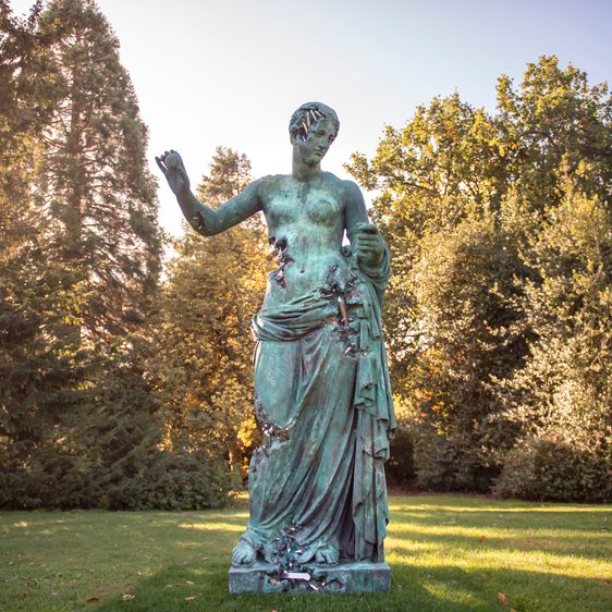 A large bronze sculpture of a woman wearing a draped robe with her arms outstretched.