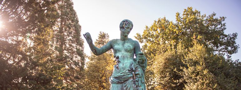 A large bronze sculpture of a woman wearing a draped robe with her arms outstretched.
