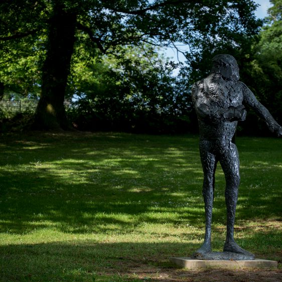 A bronze humanoid figure, displayed outdoors.