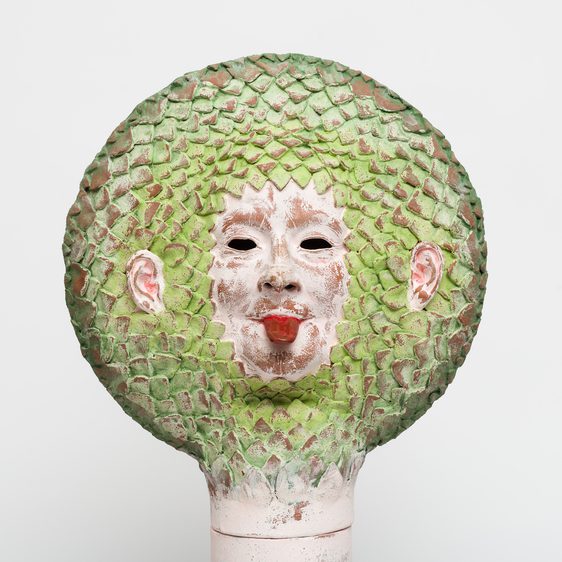 A ceramic face with it's tongue out, with green leaf-like hair.
