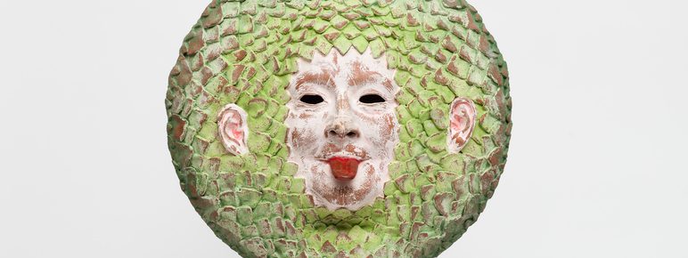 A ceramic face with it's tongue out, with green leaf-like hair.
