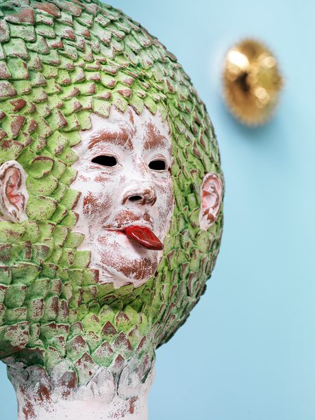 a ceramic head with green leaves surrounding it, sticking out it's tongue.