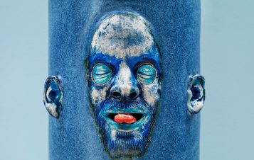 A close up of a blue ceramic cylinder with a face emerging from it.