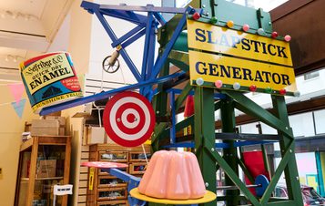 A colourful scaffolding structure with giant targets, models of jelly and paint cans. A sign reads SLAPSTICK GENERATOR