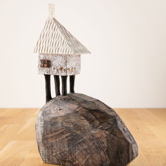 A miniature carved wooden house on top of a carved wooden mound