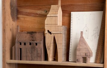 Three miniature wooden houses and a pencil drawing of a house on a shelf.