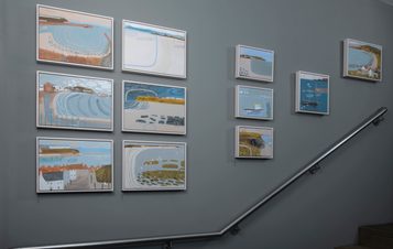 Eleven paintings hung going up a staircase.