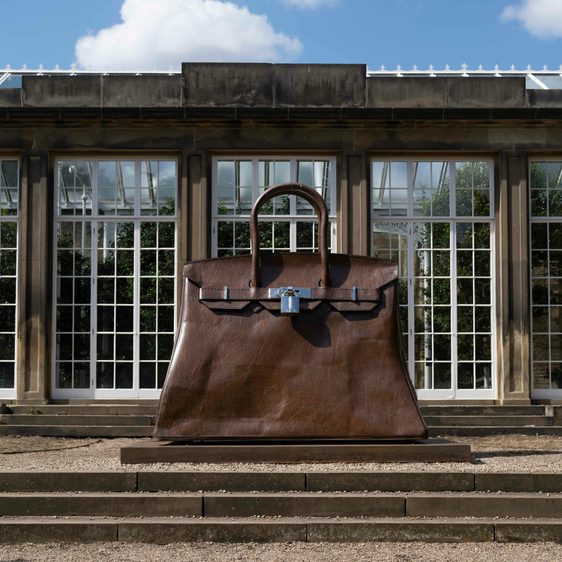 A giant brown Birkin handbag in front of a building with glass windows.