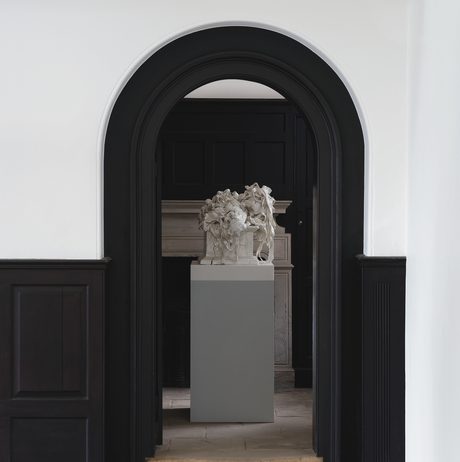 Porcelain sculpture on a plinth, framed by a black arched door way.