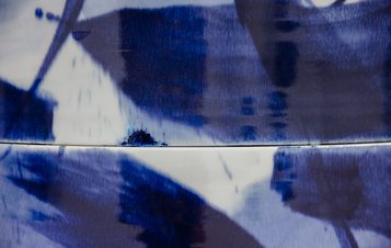 An abstract image featuring a blend of deep blue and white hues. The surface displays fluid, painterly strokes, creating a sense of movement and depth. The texture appears glossy, reflecting light and enhancing the visual complexity.