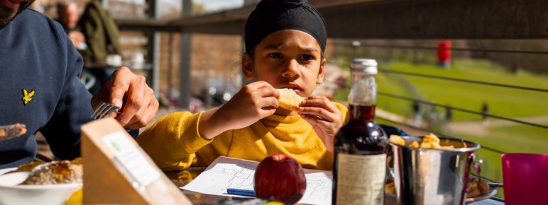 A child and father enjoying food on the balcony in the sun at YSP