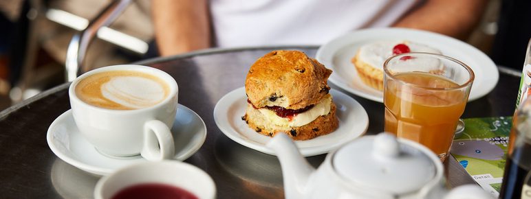 a table with cups of tea, a teapot, glass of juice and cream scone.