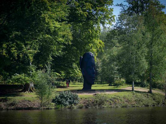 A sculpture of a girl's head flanked by trees, overlooking the lake.