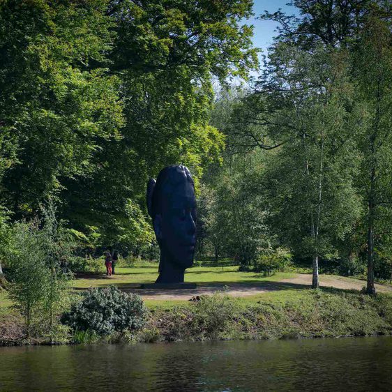 A sculpture of a girl's head flanked by trees, overlooking the lake.