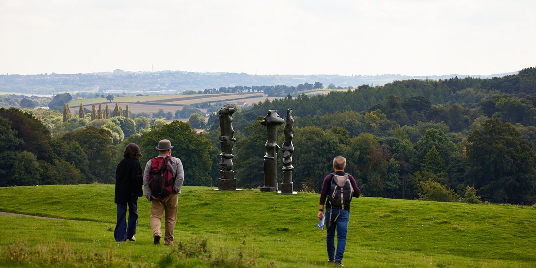 A group of people walking towards three tall thin sculptures on a hillside.