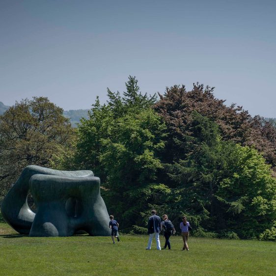 People walk across the grass in the country park towards a Henry Moore sculpture.