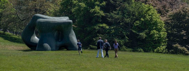 People walk across the grass in the country park towards a Henry Moore sculpture.