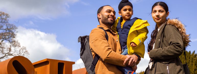 two adults and a child smiling in front of a Robert Indiana sculpture at YSP