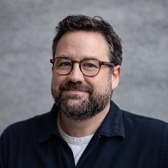 A white man with short brown hair, short beard and glasses looks directly into the camera.