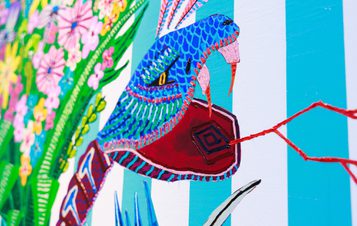 A vibrant, stylised snake with a blue and green patterned body and a red mouth is depicted against a striped background. Surrounding it are colourful flowers and foliage, creating a lively and artistic atmosphere.