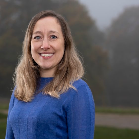 A woman with long hair is smiling wearing a blue jumper