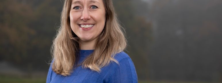 A woman with long hair is smiling wearing a blue jumper