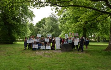 A large group of people holding hand decorated banners under the trees at YSP.