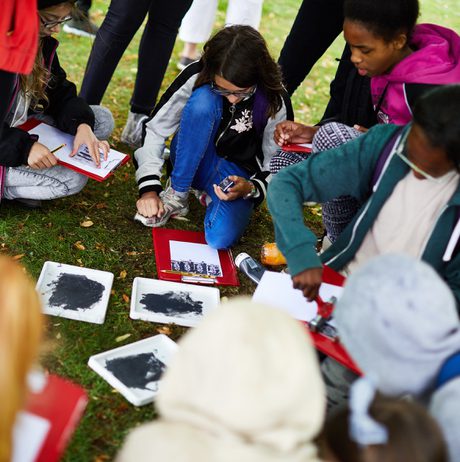 A group of young children kneeling on grass, pressing stamps onto paper.