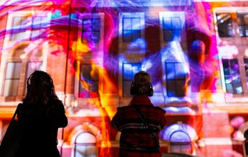 Silhouettes of two people looking up at a building with a digital artwork projected onto it.