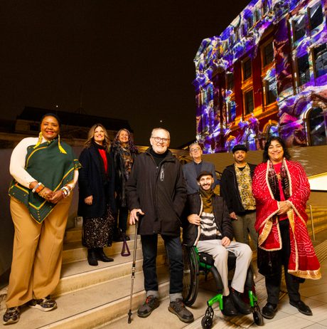 A group of people standing in front of a building with a digital artwork projected onto it.