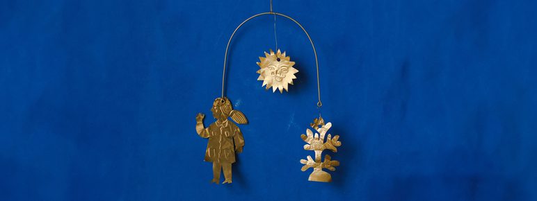 A folk-art style mobile made from shiny gold metal, featuring a person, sun and flower, against a blue background.