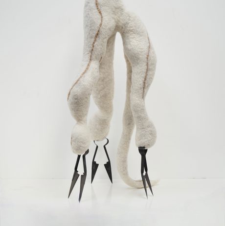 A sculptural piece crafted from soft, white wool with a brown seam. It features vintage metallic shears as feet, giving it a slightly menacing appearance against a plain white background.
