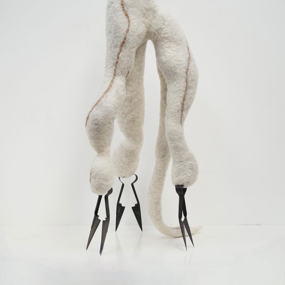 A sculptural piece crafted from soft, white wool with a brown seam. It features vintage metallic shears as feet, giving it a slightly menacing appearance against a plain white background.