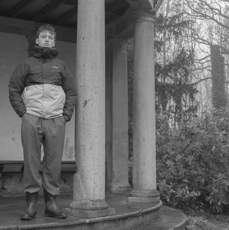 A man wearing winter clothing stands inside a folly structure with tall columns.
